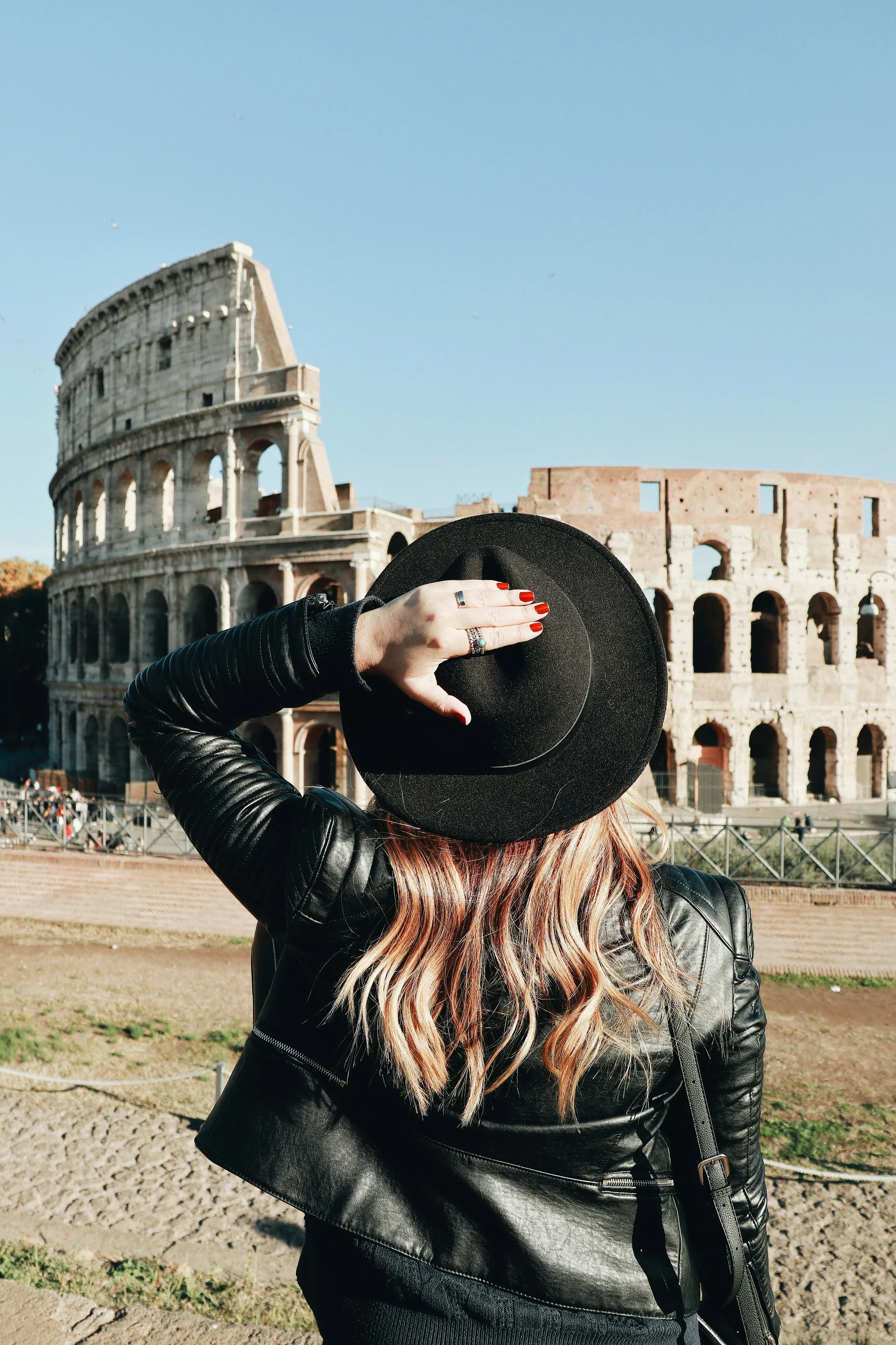 A traveller in a black hat looking towards the sunlit Colosseum